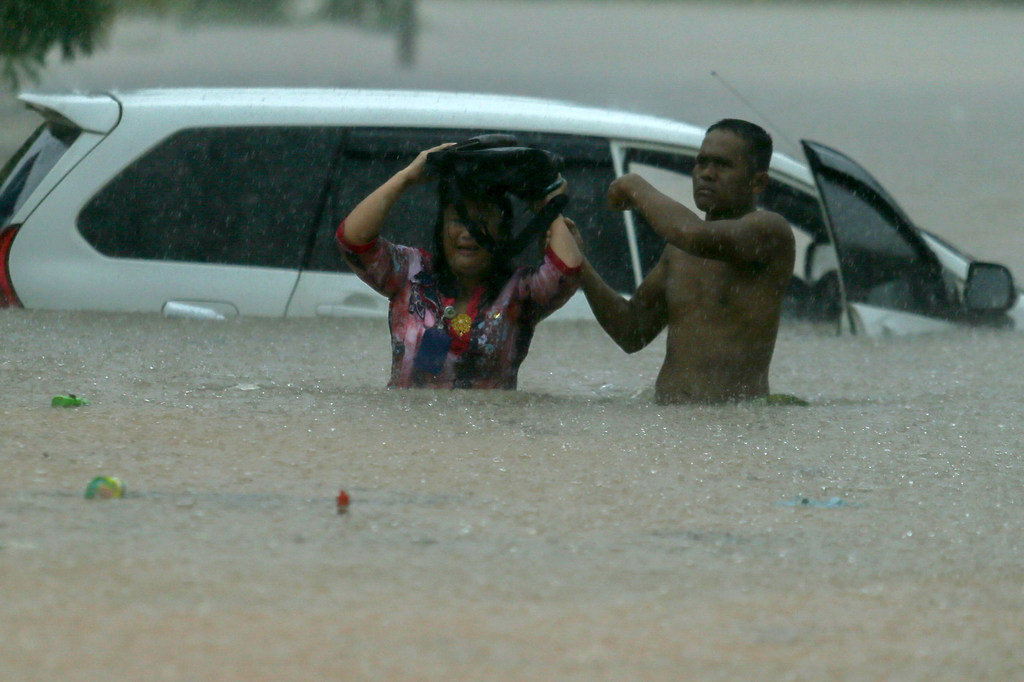 A man helps a woman after her car is stranded in waist-deep water. Globally rains are being more extreme due to impacts of climate change.